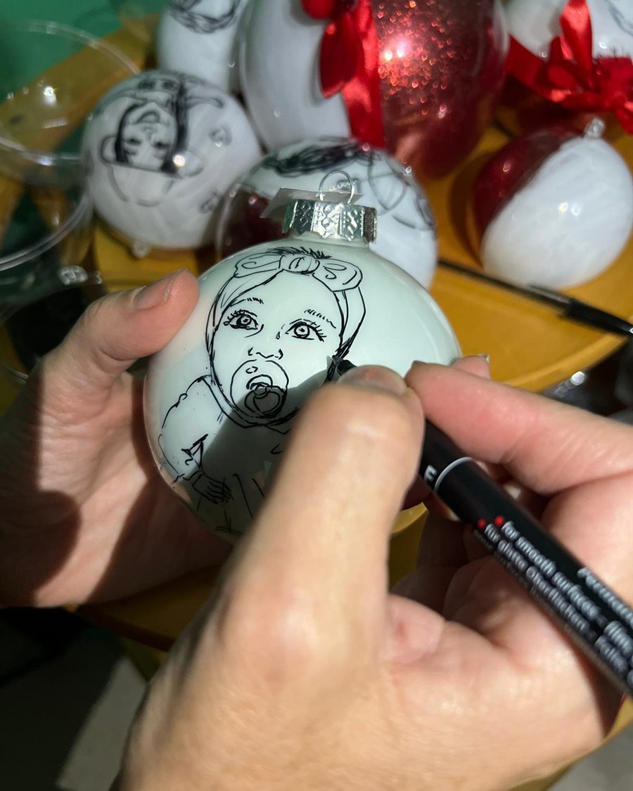 La mano dell'artista mentre dipinge un ritratto sulla superficie curva di una pallina di Natale